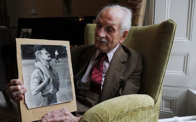 Paddy Hemingway at home holding photo of himself in uniform in RAF