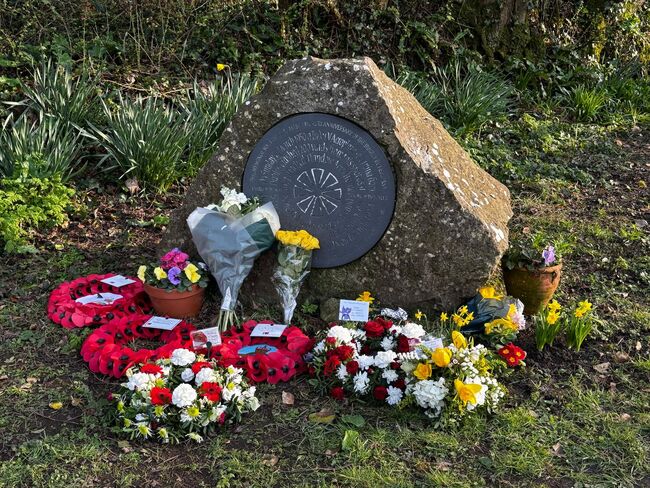 Flowers and wreathes in front of plaque memorial on stone